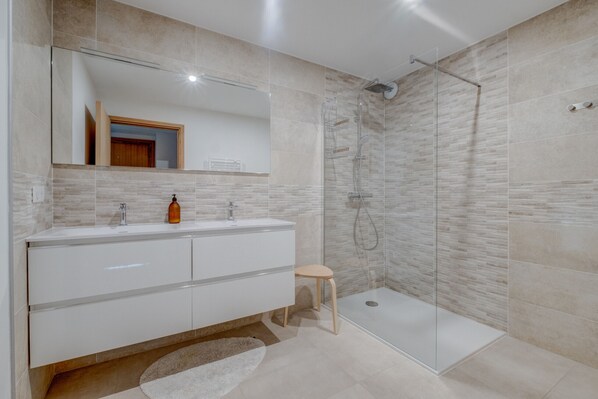 Une salle de bain moderne avec une douche à parois de verre, un meuble-lavabo blanc avec un miroir et un petit tabouret.