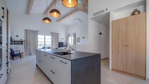 Een moderne keuken met een centraal eiland, hangende lampen en een houten kledingkast.