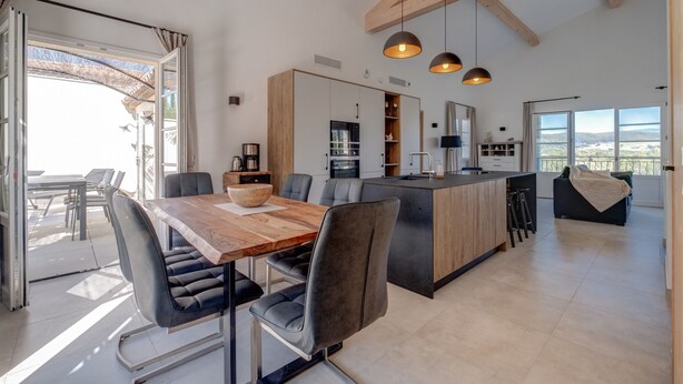 Een moderne keuken met een centraal eiland, hanglampen en een eethoek met een houten tafel en stoelen.