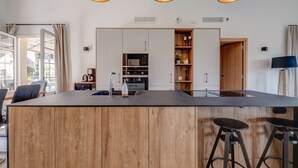 Een moderne keuken met een centraal eiland, houten kastjes en hangende verlichting.