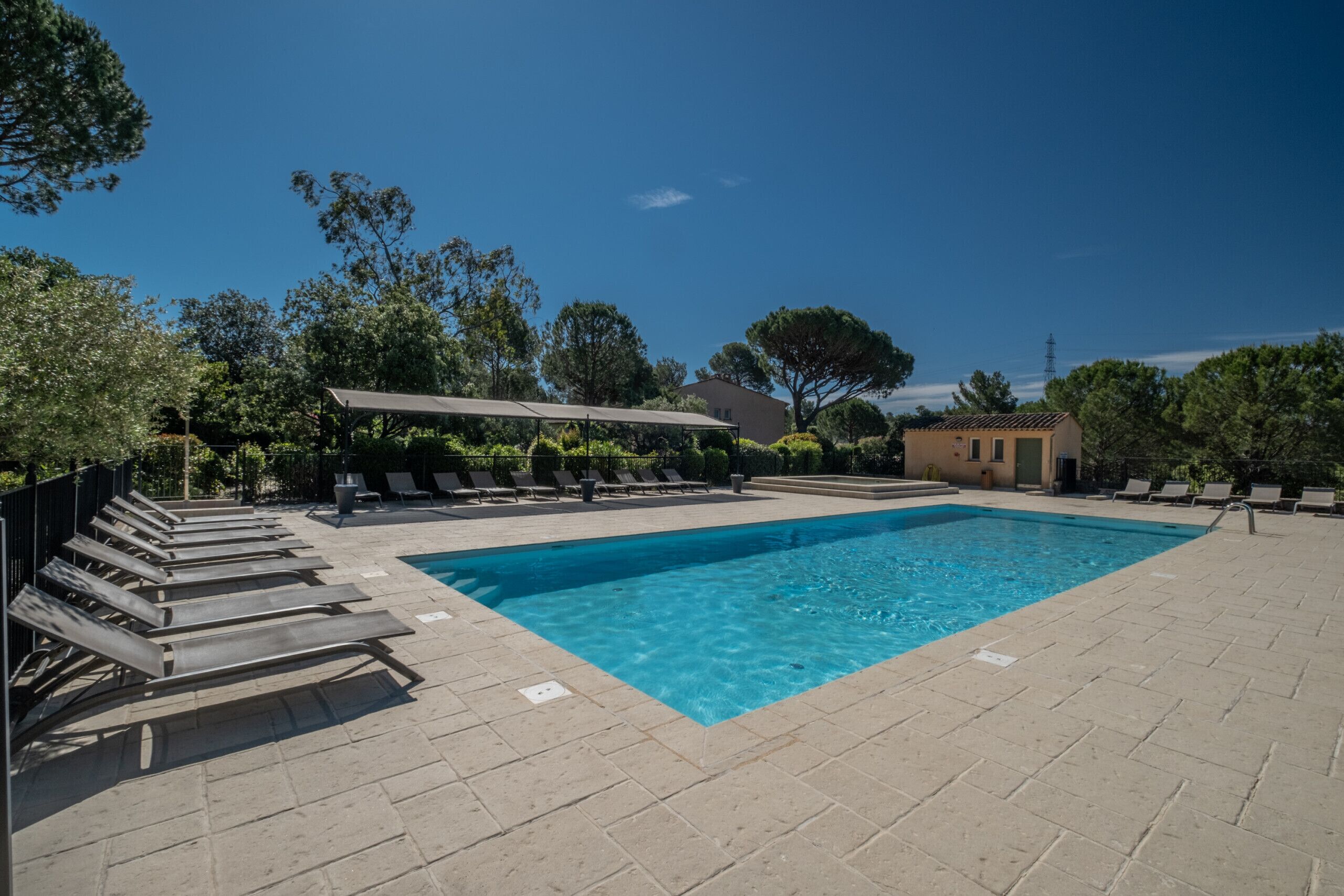 Una piscina rectangular con agua cristalina azul, rodeada de tumbonas y un área de estar cubierta.