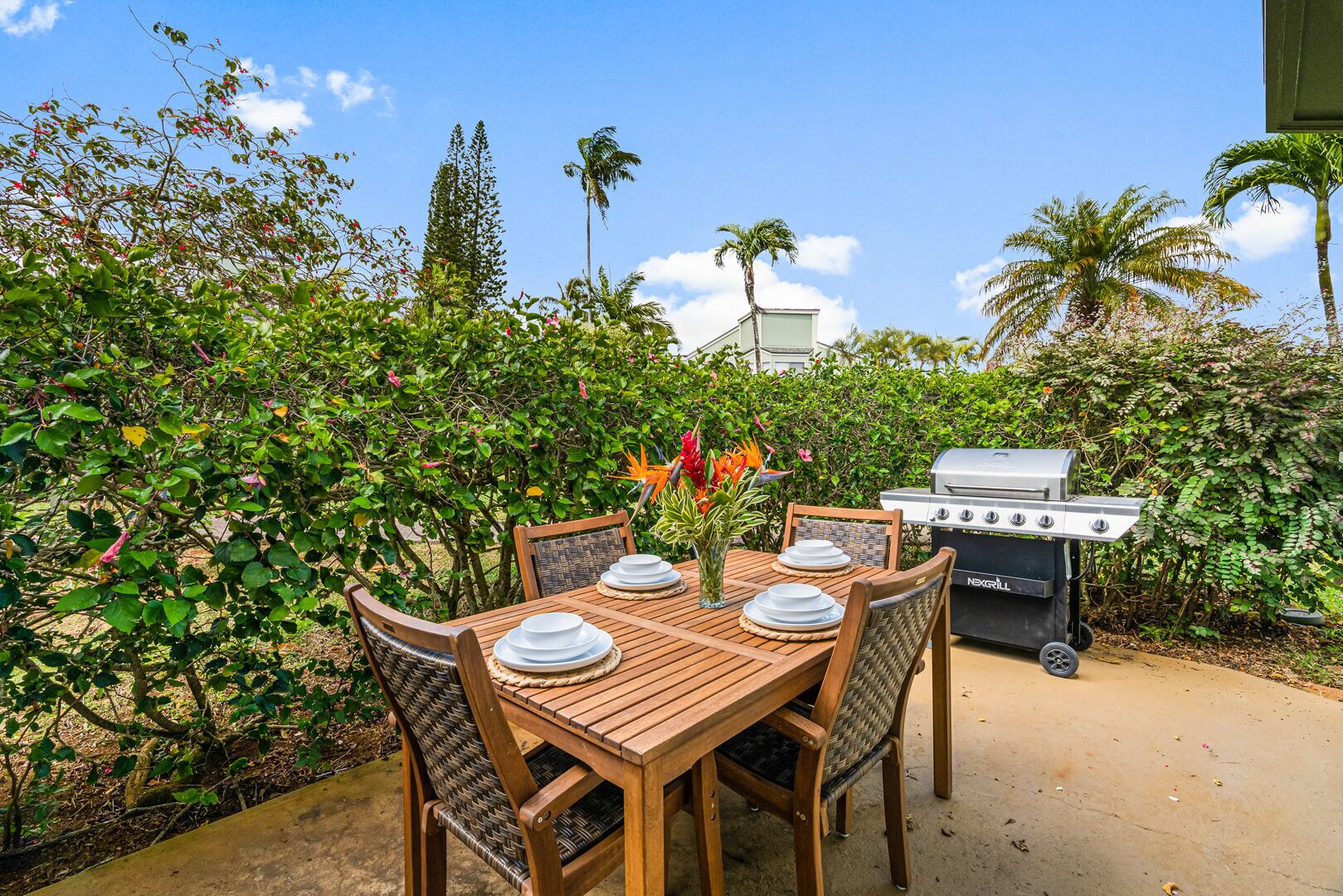 Un espace de restauration en plein air avec une table en bois prévue pour quatre personnes, entourée d’une végétation luxuriante et agrémenté d’un barbecue.