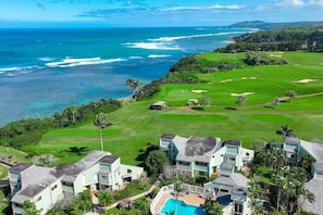 Um campo de golfe com vista para o oceano, rodeado por vegetação exuberante e edifícios modernos.