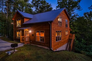 A two-story log cabin with a metal roof, a front porch, and a staircase leading to the upper level. - Game Room, Hot Tub, & 3 King Beds, Dogs Welcome (Sevierville)