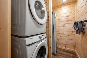 Uma área de lavanderia compacta, com máquina de lavar e secadora Samsung, paredes de madeira e um porta-toalhas.