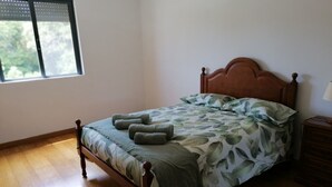 Een enkel bed met een houten hoofdbord, een beddegoed met groene bladprint en twee opgerolde handdoeken op het bed.
