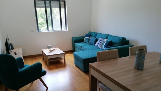 Een woonkamer met een blauwgroene bank, een houten salontafel en een eettafel met stoelen.