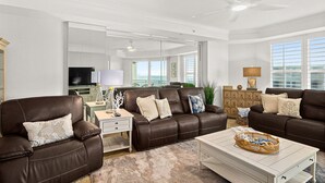 A spacious living room with a brown leather sofa set, a white coffee table, and a large mirror reflecting the room.