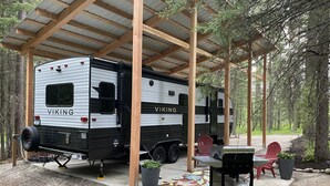 A covered RV park with a Viking RV, outdoor seating, and a barbecue area.