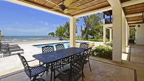 Ein überdachter Außenbereich mit Pool, Sitzgelegenheiten und Blick auf den Strand.