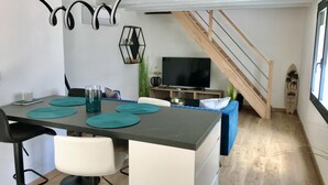 A modern kitchen with a dining table, chairs, and a TV in the background. - Les Cocons du Bassin - Cocon Duplex&design - Clim/wifi/linge Compris (Gujan-Mestras)