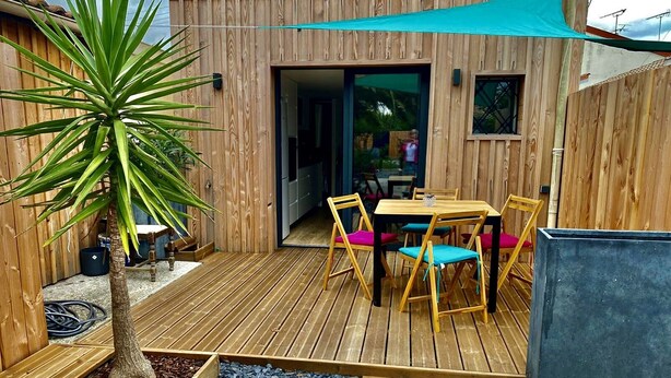 A wooden deck with a table and chairs, a sliding glass door, and a small plant. - Les Cocons du Bassin - Cocon Duplex&design - Clim/wifi/linge Compris (Gujan-Mestras)