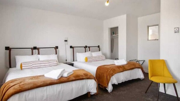 A hotel room with two beds, a yellow chair, and a wardrobe. - Fillmore Lodge: Discounted 2 Double Queens Rm (Fillmore)