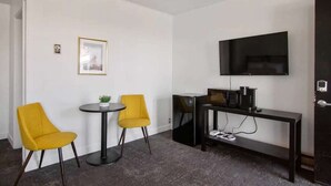 A modern room with a flat-screen TV mounted on the wall, two yellow chairs, a small round table with a plant, and a black console table with electronic devices. - Fillmore Lodge: Discounted 2 Double Queens Rm (Fillmore)