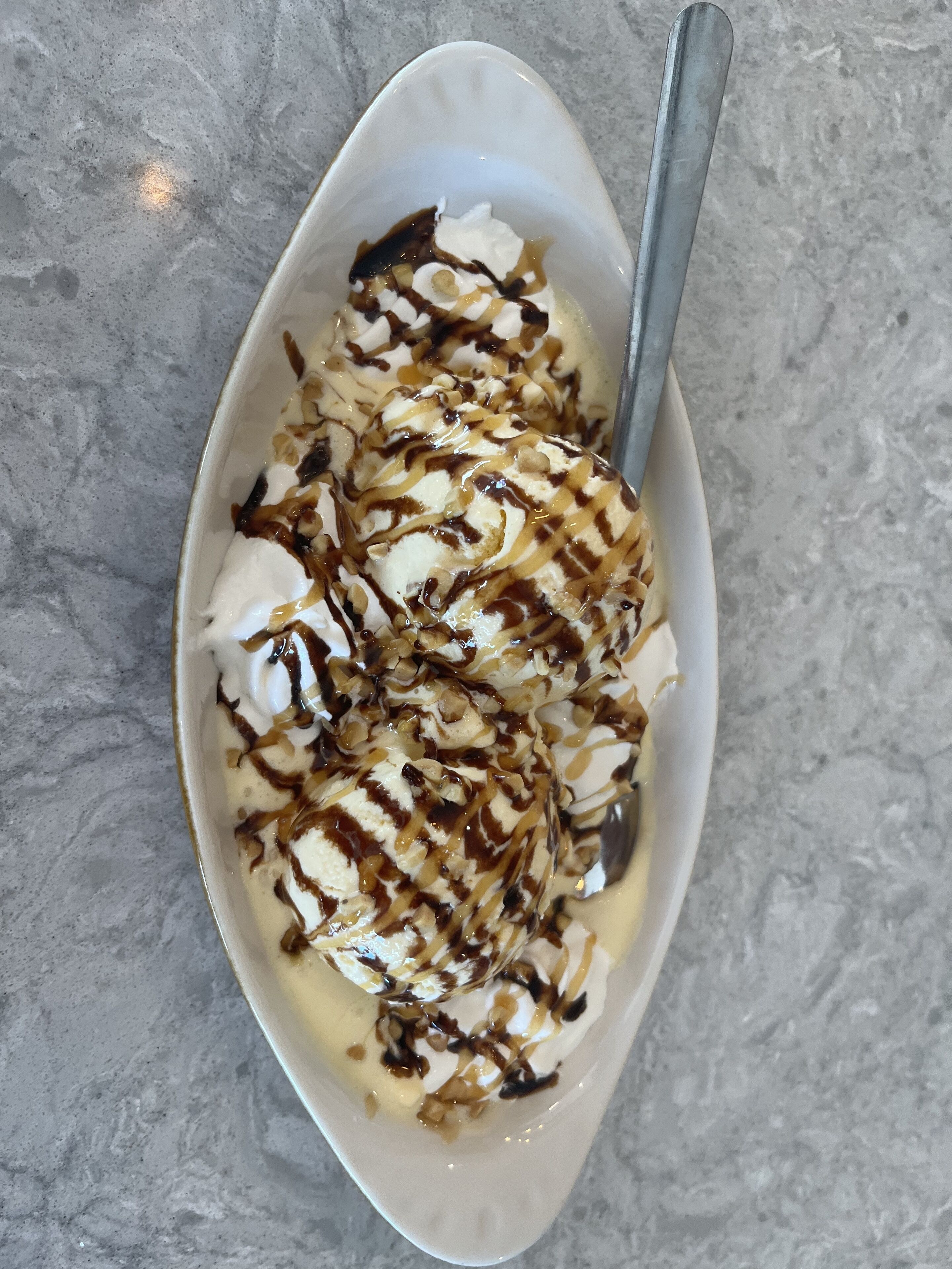 Un bol de postre con crema batida, caramelo y salsa de chocolate.