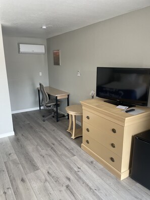 A small, well-lit room with a wooden floor, a beige dresser with drawers, a television on top, a small round table, and a chair. - Sunglow Hotel (Bicknell)