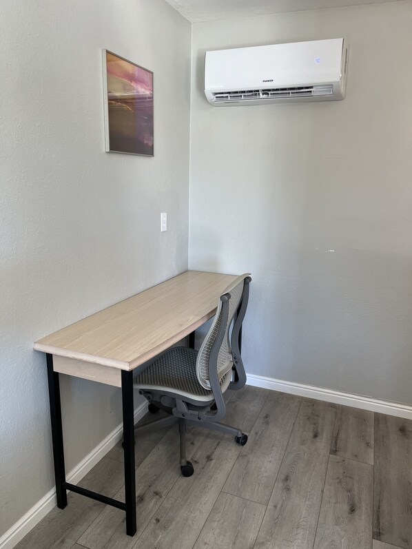 A room with a wooden desk, a gray office chair, and an air conditioning unit mounted on the wall.