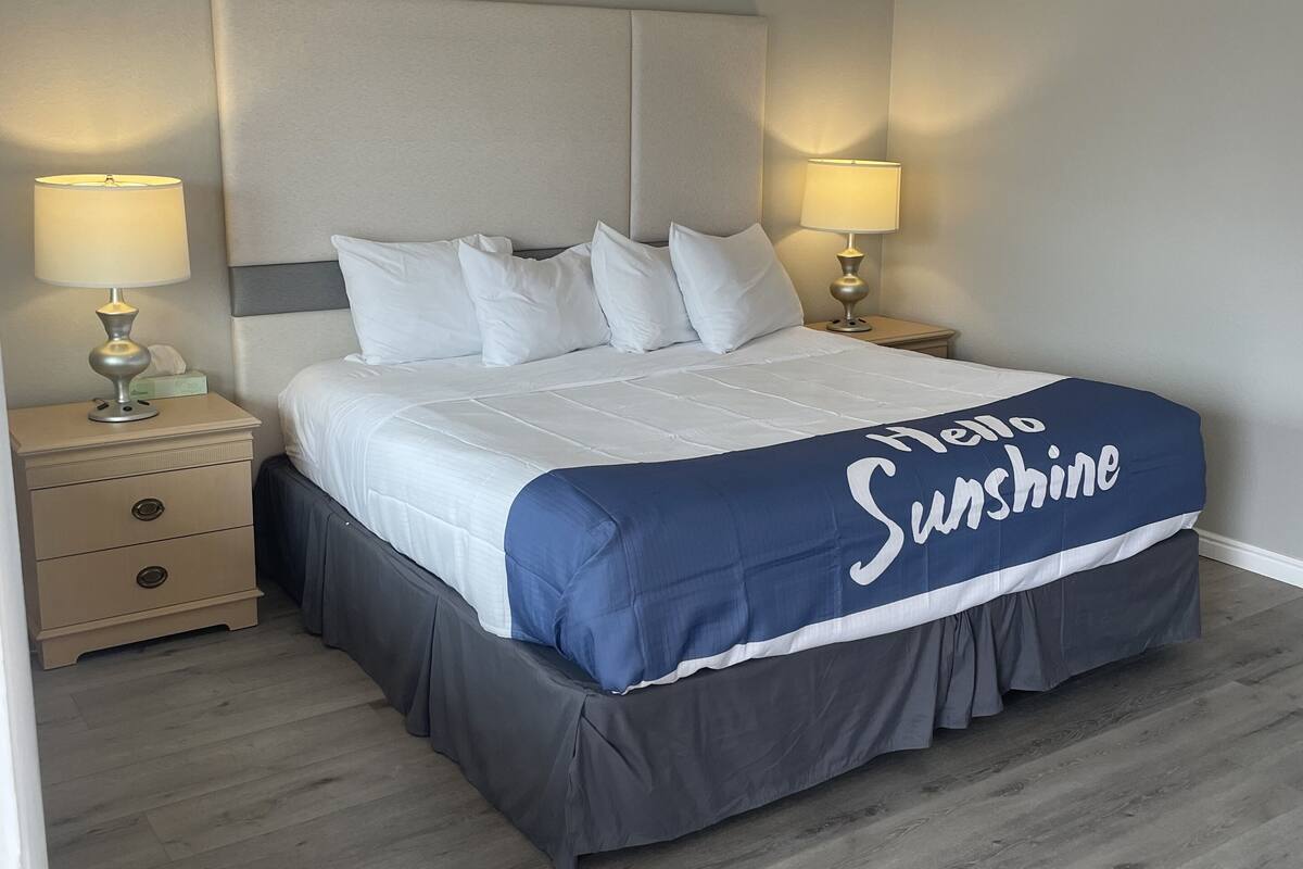A neatly made bed with a blue and white cover, two bedside lamps, a wooden nightstand, and a headboard.