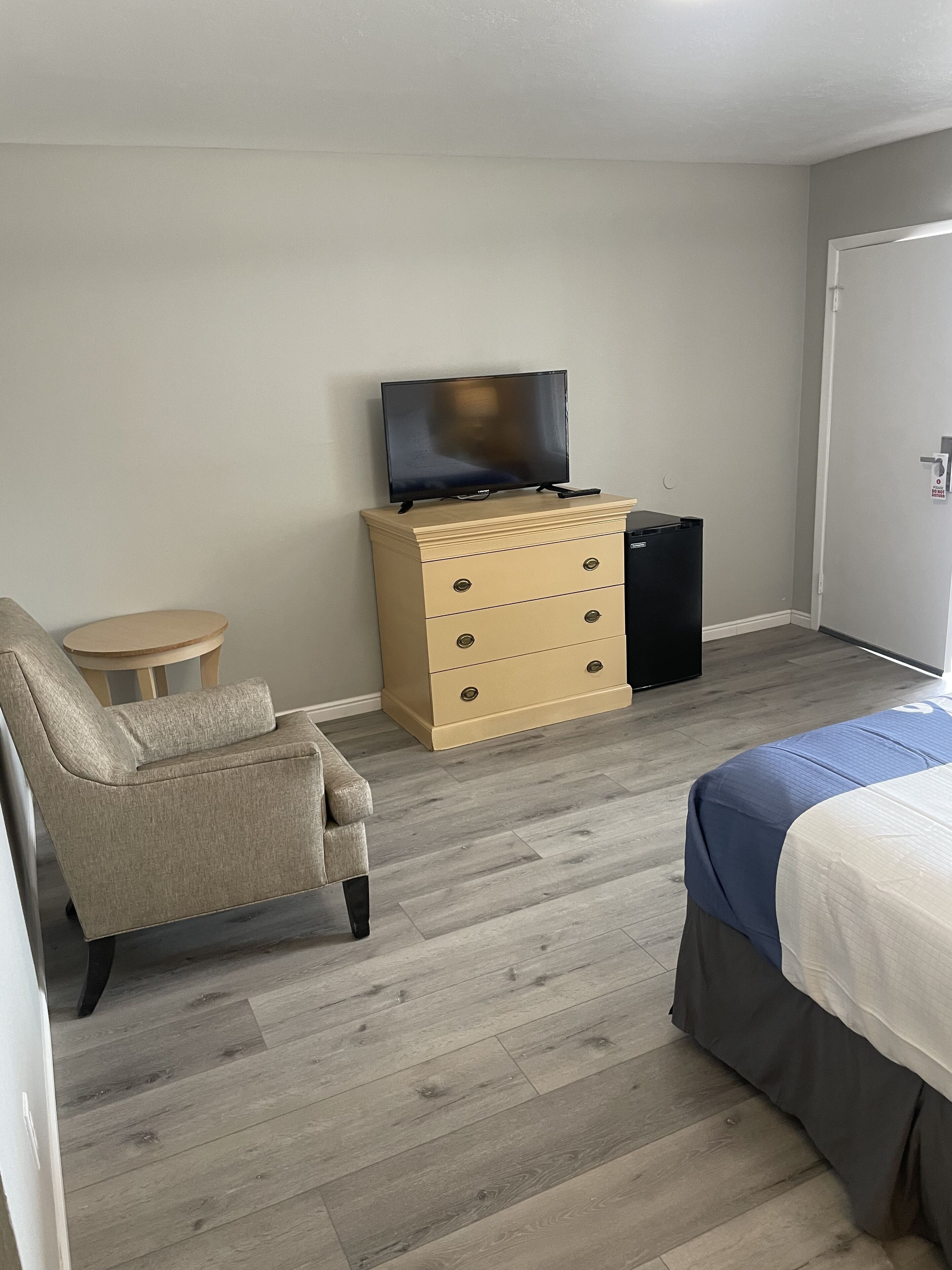 A hotel room with a bed, a chair, a dresser, a television, and a small table.