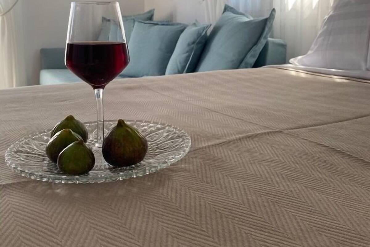 A bed with a glass of red wine and figs on a clear glass plate.