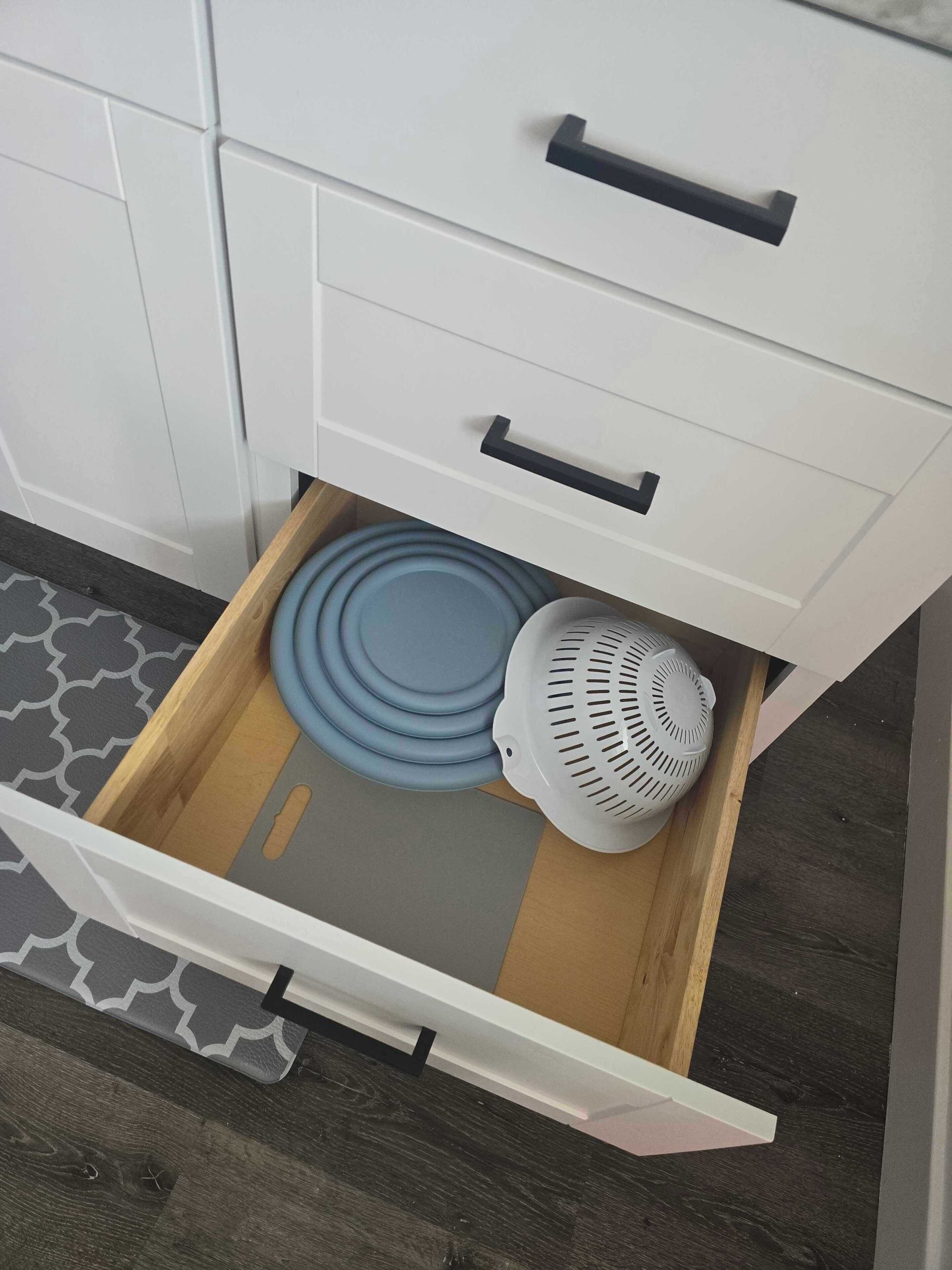 Un cajón de cocina con un colador azul y un escurridor blanco.