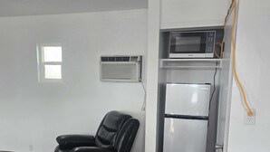 A compact kitchen with a refrigerator, microwave, and air conditioning unit.