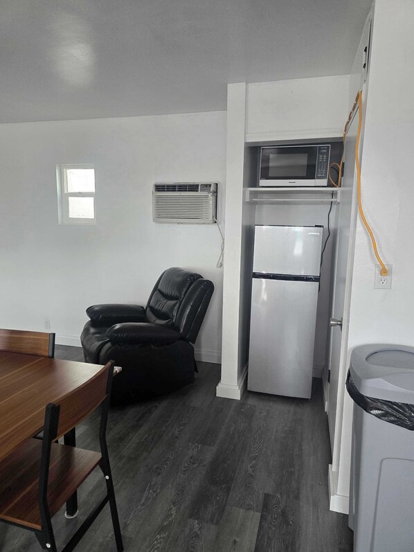 A compact kitchen with a refrigerator, microwave, and air conditioning unit.