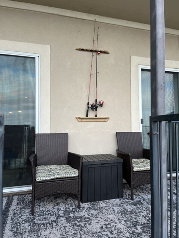 A balcony with two wicker chairs and a small table, a fishing rod mounted on the wall, and a glass door. - WATERFRONT 2/2 CONDO BOAT DOCK/SLIP RESTAURANT KAYAK AMENITIES GRD. FL Sleeps 8 (Willis)