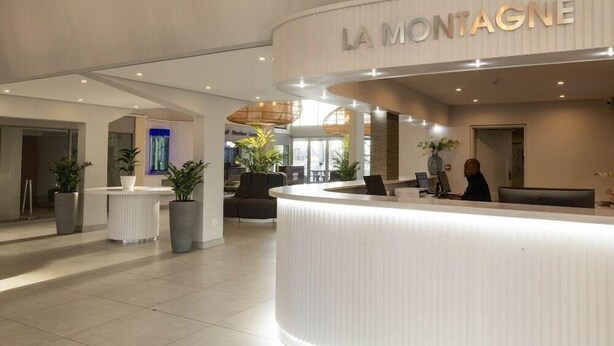 A modern hotel reception area with a curved reception desk, potted plants, and a seating area. - La Montagne (Ballito)
