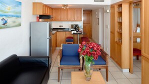 A compact living space with a kitchenette, a dining area with two blue cushioned chairs, a black sofa, and a table with a vase of red roses. - La Montagne (Ballito)
