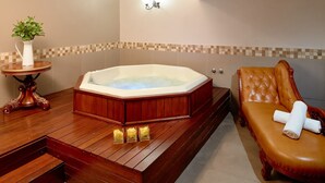 A bathroom with a wooden bathtub, a cushioned bench, a small table with a vase, and a wall-mounted light fixture. - La Montagne (Ballito)