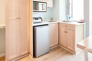 A compact kitchen with wooden cabinets, a built-in microwave, a refrigerator, and a window providing natural light.