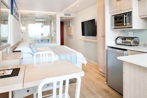 A compact hotel room with a bed, a small dining table, a kitchenette with a microwave, and a TV mounted on the wall.