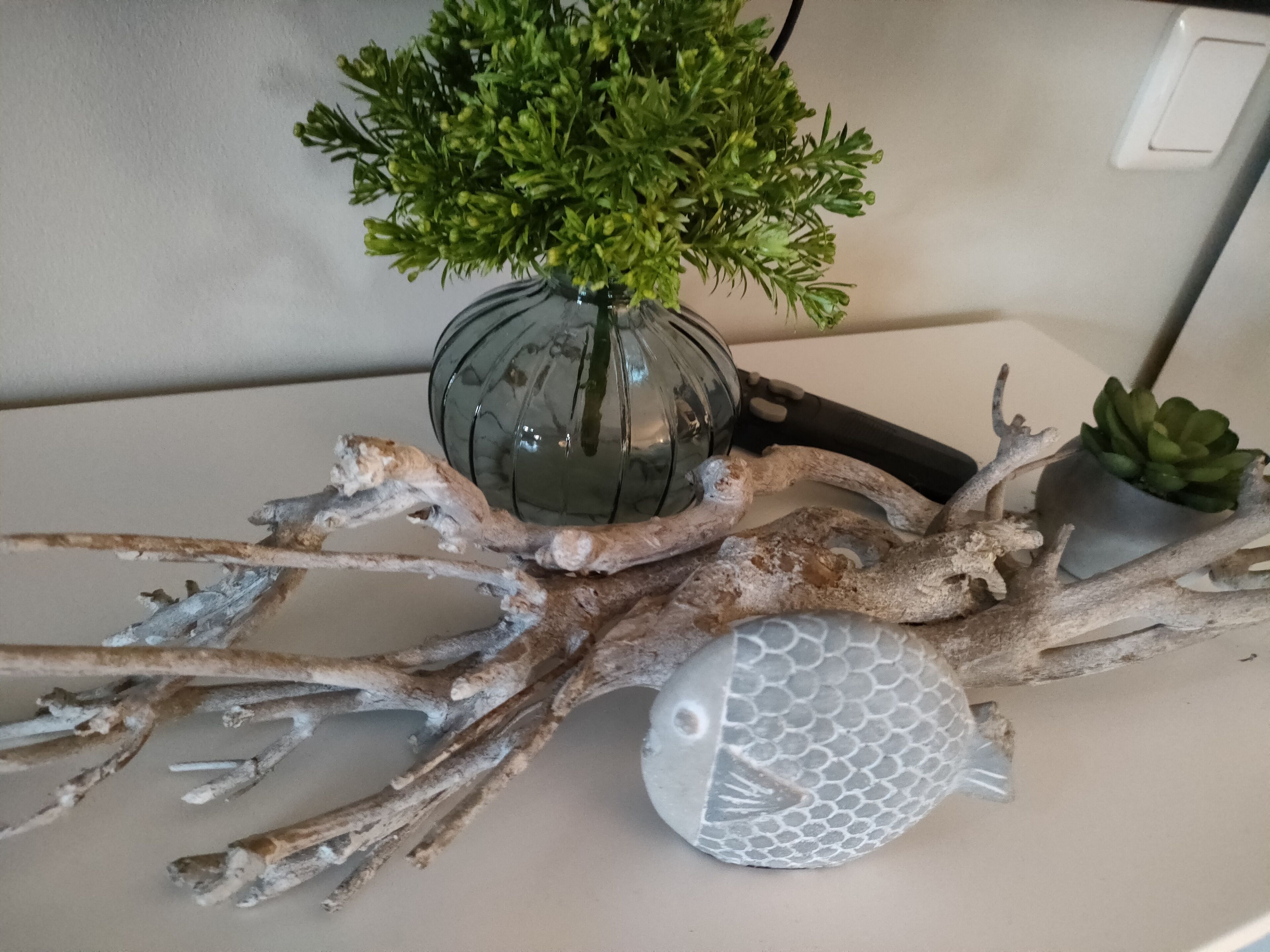 A decorative arrangement with a glass vase, a succulent, and a fish sculpture on a branch.