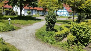 A garden path leading to traditional buildings with red roofs, surrounded by lush greenery and trees. - Rugiamare, Exclusives, neu Renoviertes, Strandnahes Reihen- Ferienhaus (Dranske)
