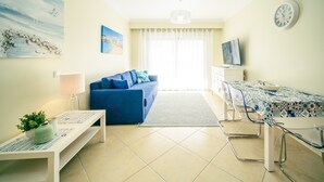 A modern living room with a blue sofa, a dining table with chairs, a TV, and artwork on the walls.