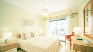 A hotel room with a bed, a desk with a lamp, a chair, a map on the wall, and a view of the outside.