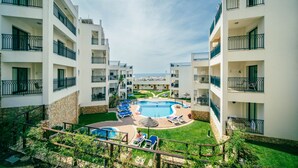 A hotel with a central swimming pool surrounded by lounge chairs and a small garden area.