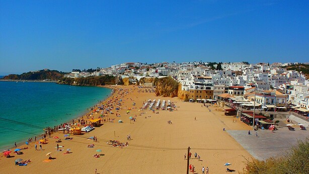 A beach with a clear view of the sea and a densely packed town in the background.
