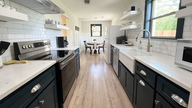 A modern kitchen with white and black cabinetry, stainless steel appliances, and a wooden floor.