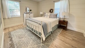A bedroom with a bed, nightstands, a dresser, a ceiling fan, and a window with curtains.