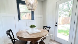 A dining area with a round wooden table, two black chairs, and a white chair. A woven pendant light hangs above the table.