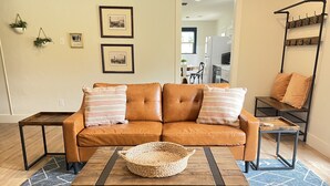 A living room with a brown leather sofa, two striped pillows, a woven basket on a wooden coffee table, and a blue patterned rug.