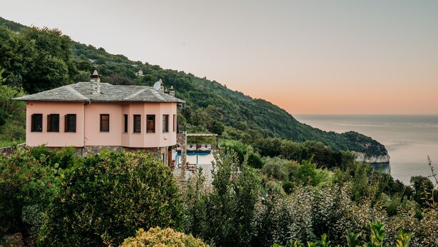 Une villa rose avec piscine, entourée d’une végétation luxuriante et offrant une vue sur la côte.