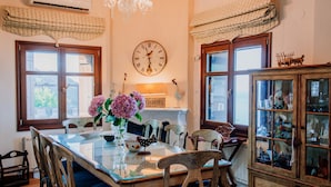 Une salle à manger avec une table en verre, des chaises en bois, un lustre et une horloge au mur.