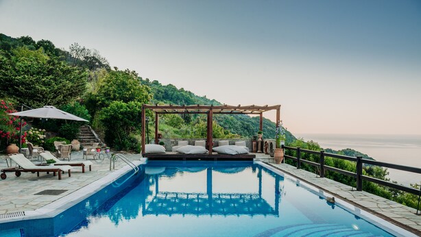 Une piscine agrémentée d’une pergola en bois et de chaises longues, entourée de carreaux de pierre et de verdure.
