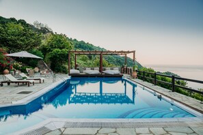A pool with a wooden pergola and lounge chairs, surrounded by stone tiles and greenery. - Elysian Luxury Villa Pelion (Zagora-Mouresi)