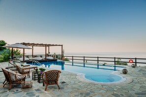 A poolside area with lounge chairs, a pergola, and a view of the ocean. - Elysian Luxury Villa Pelion (Zagora-Mouresi)