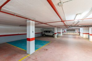 An indoor parking garage with concrete floors, red and white pillars, and a white car parked in one of the bays.