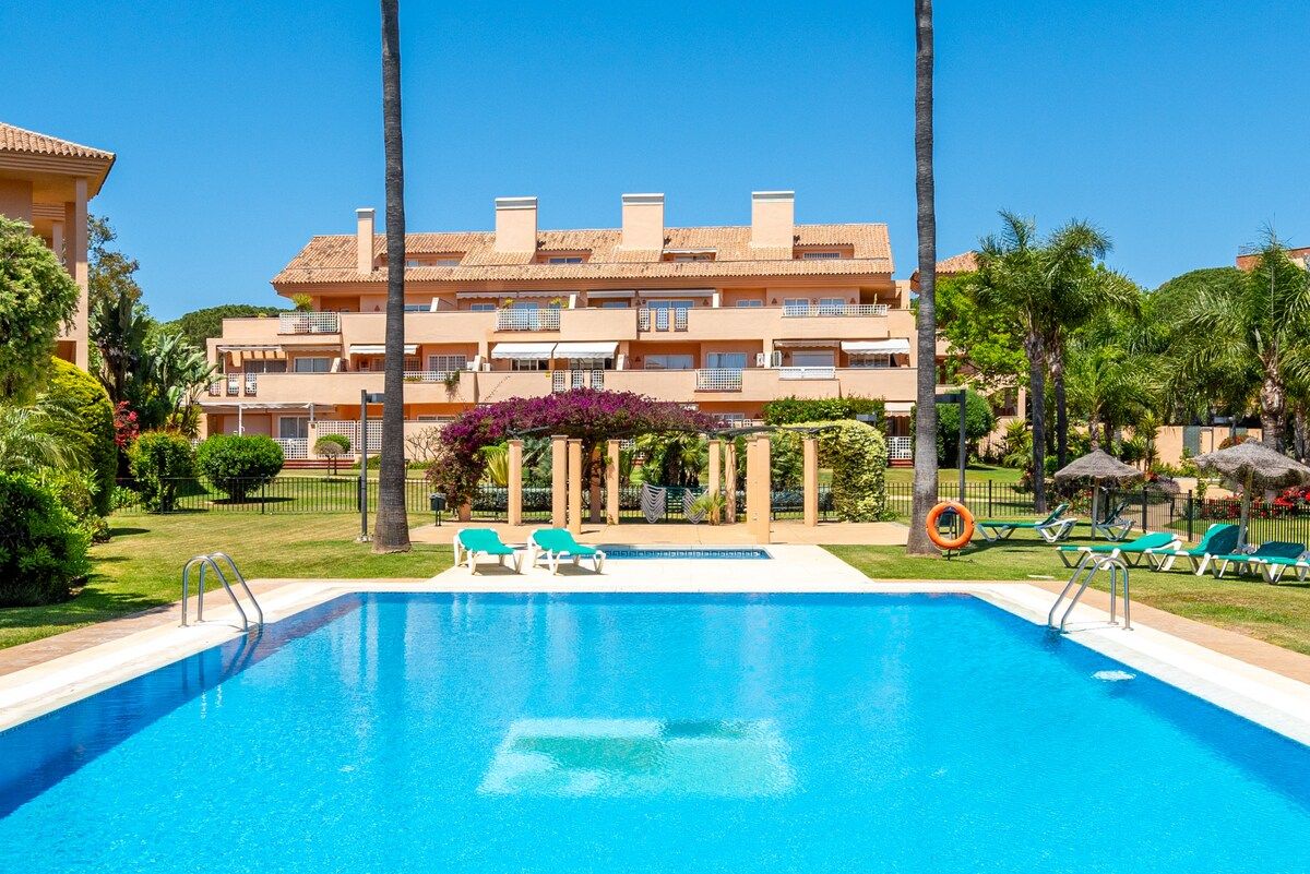 A swimming pool with lounge chairs and a building with balconies in the background.